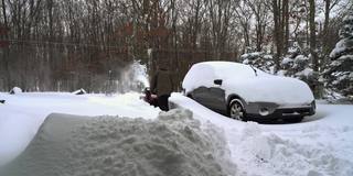 一场冬季暴风雪过后，一名男子正在清理他被雪覆盖的汽车周围的车道。