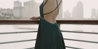 一位身穿绿色晚礼服的年轻亚洲新娘，站在湖滨码头，以城市建筑为背景，微笑着看着镜头，用慢镜头拍摄