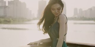 一位身穿绿色晚礼服的年轻亚洲新娘，站在湖滨码头，以城市建筑为背景，微笑着看着镜头，用慢镜头拍摄