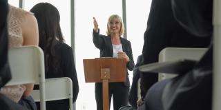 资深女商人站在讲台上发表演讲，在研讨会上发言。在“办公室会议”中听取同事们的问题