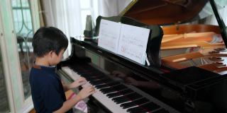 亚洲男孩在客厅里弹三角钢琴，看着音符。孩子专心练习。业余爱好和在家学习。快乐的一天和家庭的概念。活动和生活方式。