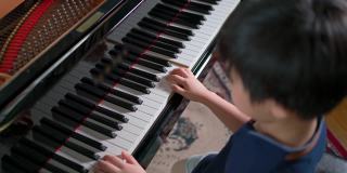 俯视图亚洲男孩在客厅弹奏三角钢琴和选择性的焦点在手上。在线练习和学习。业余爱好和在家学习。快乐的一天和家庭的概念。活动和生活方式。