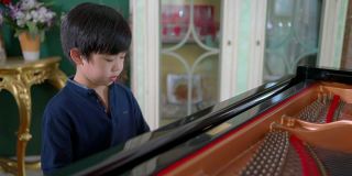 亚洲男孩在客厅里弹奏三角钢琴。孩子感到高兴和实践课。业余爱好和在家学习。快乐的一天和家庭的概念。活动和生活方式。
