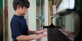 侧视亚洲男孩在客厅里弹钢琴。有选择性的重点。孩子专心上课。业余爱好和在家学习。快乐的一天和家庭的概念。活动和生活方式。