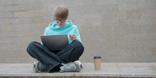 一名年轻女子在网上视频通话时写博客。她坐在户外，拿着笔记本电脑和朋友聊天