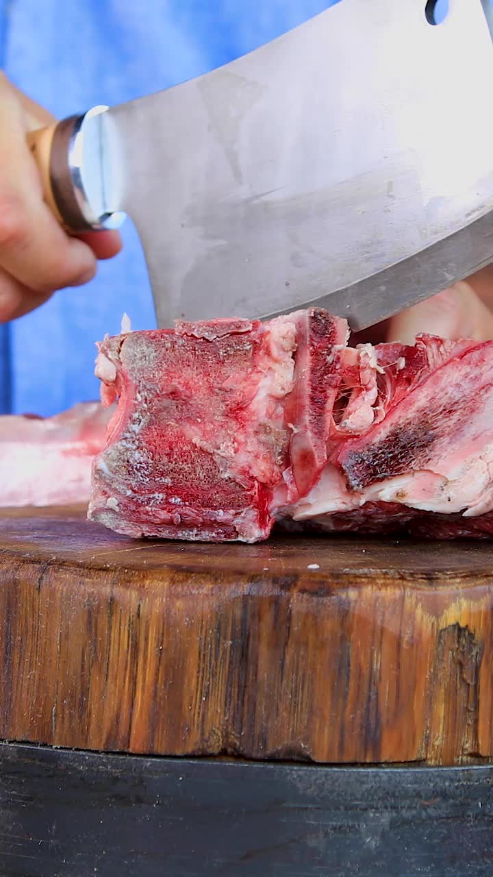 一名男子用刀在一块砧板上切生肉。砧板上的新鲜肉。特写镜头