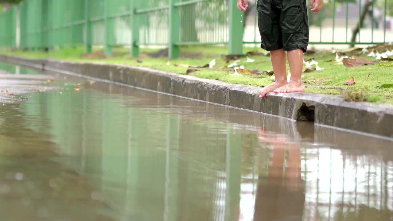 慢动作蹒跚学步的男孩在村里的路上的水坑上跳