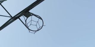 在篮球场上，一个篮球穿过一个有金属链网的篮筐。背景是天空和云彩