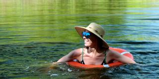 一名身穿泳衣、头戴草帽的女子带着一个充气圈漂浮在湖、河的池塘里。女孩休息在游泳池游泳圈与蓝色的水