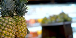 一位女士在超市里挑选菠萝。在水果店购物。女性持有