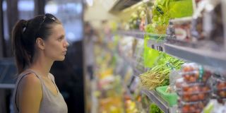 妇女在有机蔬菜部冰箱里挑选生菜。购买健康的素食