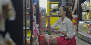 一位年轻的美国妇女正坐在超市的地板上挑选女性卫生用品垫