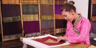 工艺品和工艺。亚洲妇女在丝绸上绣金线。年轻的女人在缝丝绸。