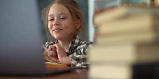 在笔记本电脑上通过视频电话会议在线学习时，微笑的小学女孩与在线老师交谈的特写。