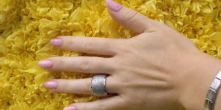 一位漂亮的女性手修得很好，手上戴着昂贵的戒指，手指在黄色的花瓣上划过
