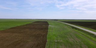 沿途的农田全景，远处的拖拉机用专用设备犁耕耙地，为季节性小麦播种准备土壤，由无人机从高空拍摄
