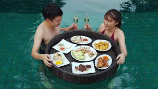 幸福的年轻夫妇享受着漂浮的食物，在游泳池里喝着香槟杯视频素材模板下载