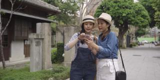 快乐的女游客走在街上在日本京都的日本老城区寻找网上交易的假期。两个女友自导旅行。年轻女子讨论在线地图手机