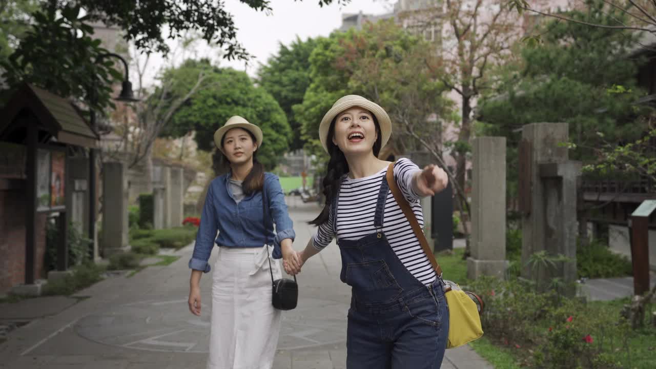 两个亚洲女孩的朋友走在日本东京的日本街上旅行。兴奋的女人跑得飞快，手牵着手，姐妹们指着天空，惊讶地看着眼前的景色。