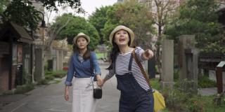 两个亚洲女孩的朋友走在日本东京的日本街上旅行。兴奋的女人跑得飞快，手牵着手，姐妹们指着天空，惊讶地看着眼前的景色。