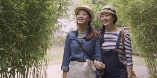 两位年轻的亚洲女性游客在自然森林中漫步，指着并谈论周围的环境。在日本大阪的竹林里，女友们悠闲地聊天。美丽最好的姐妹牵着手走