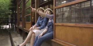 两个年轻的亚洲女性朋友坐在木制的日本风格的房子里，呼吸着新鲜的空气，一边聊天一边指着天空。女游客在京都的生活方式