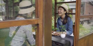 两个微笑的亚洲女性朋友在日本京都旅行，体验日本文化的秋道仪式。年轻的女孩游客聊天，喝茶，戴着草帽，坐在木桌旁边