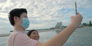 亚洲的孩子们戴着口罩一起在海滩上自拍与日出，生活理念。