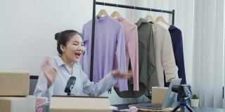 年轻的亚洲企业家正在挑选自己的衣服，通过在线电话销售向客户展示。