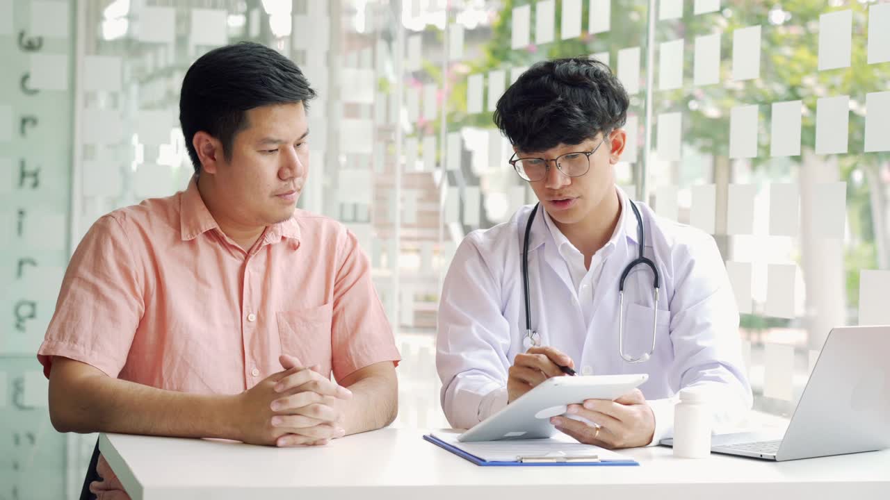 亚洲医生在诊所边用药片边和病人交谈，解释病人的病情和治疗结果。