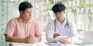 亚洲医生在诊所边用药片边和病人交谈，解释病人的病情和治疗结果。