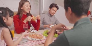 亚洲幸福家庭，年轻夫妇一起在家里举行节日聚会。漂亮迷人的父母在餐桌上碰杯，吃着传统的庆祝晚餐。
