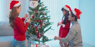 亚洲可爱的家庭成员用幸福装饰圣诞树。年幼的女儿心情愉快，兴奋地和父母一起在家里庆祝节日圣诞节感恩节聚会。