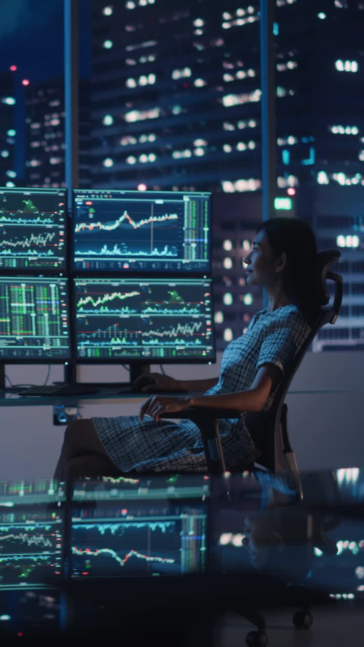 金融分析师在电脑上工作的垂直肖像与多显示器工作站与实时股票，商品和交易市场图表。在投资机构工作的女商人。