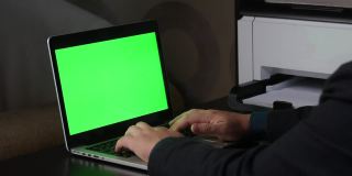 一名男子在一台绿色屏幕的笔记本电脑前工作。竖起大拇指的手势。Chromakey。