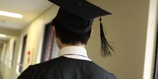 亚洲学生戴着学士帽，穿着学位服走在走廊上