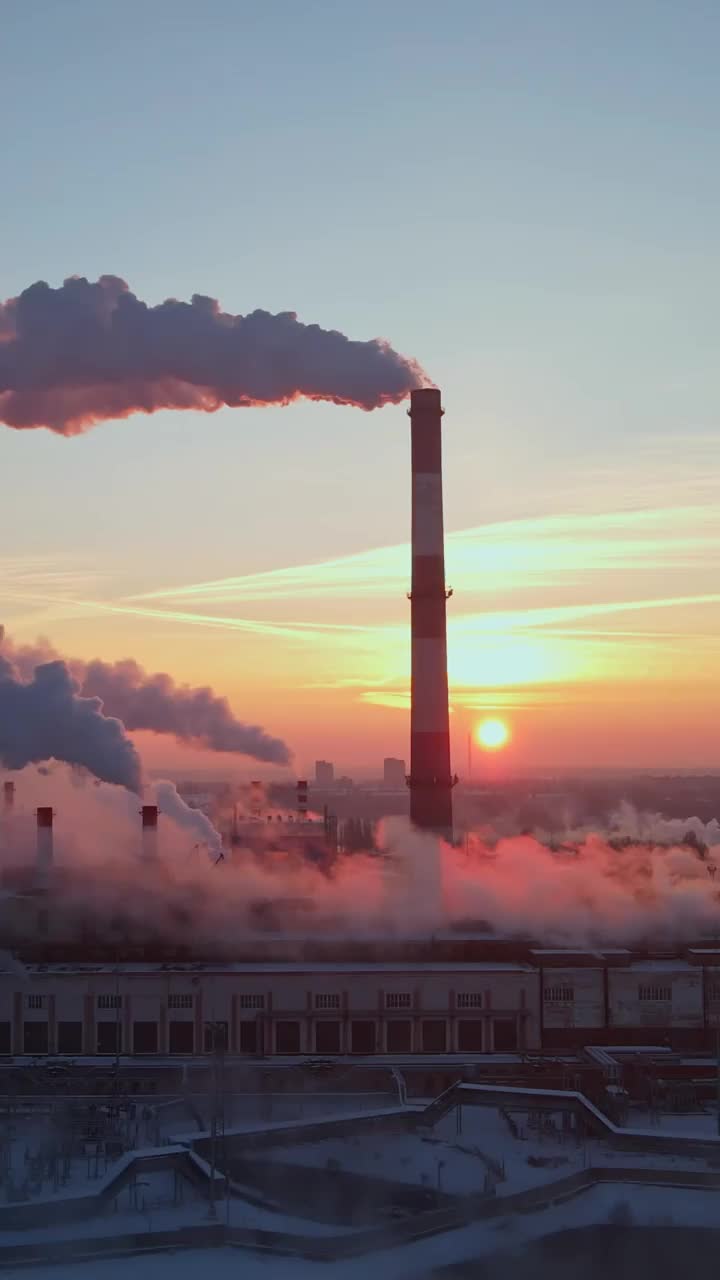 工厂的烟囱在日出时产生烟雾。垂直视频