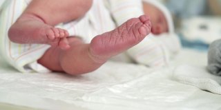 可爱的小婴儿光脚和脚趾头的第一天的生活在白色的背景。婴儿小腿干燥皮肤的特写。妈妈在换尿布的桌上换尿布。童年,孕妇的概念。