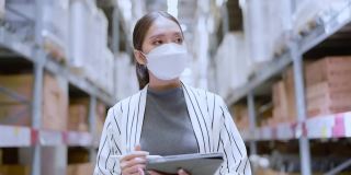 亚洲女企业主戴着口罩，用数码平板电脑检查库存产品库存数量在配送仓库工厂。物流业务运输和配送服务