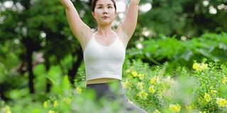 年轻的亚洲女人在花园里练习瑜伽。女性的幸福。模糊的背景。健康的生活方式和放松的观念。年轻的亚洲女孩在公园里做瑜伽。