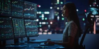 金融分析师的肖像工作在计算机与多显示器工作站与实时股票，商品和交易市场图表。在投资经纪公司工作的女商人。