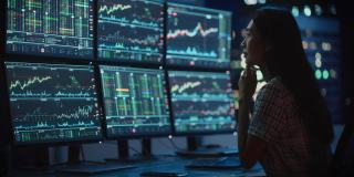 金融分析师的肖像工作在计算机与多显示器工作站与实时股票，商品和交易市场图表。在投资经纪公司工作的女商人。
