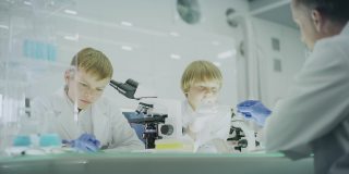 好奇的男孩在实验室工作。使用显微镜和准备实验。和父亲一起学习，传递样本