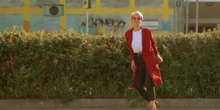 酷酷的嬉皮士сaucasian女学生穿着红色外套，戴着红色圆眼镜在城市的街道上跳舞