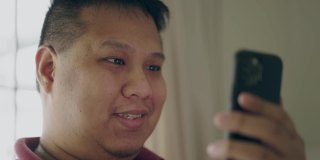 一名亚洲男子微笑着用手机进行视频通话