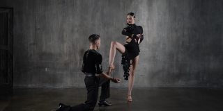 年轻优雅的千禧一代舞蹈舞厅夫妇在黑色礼服在垃圾摇滚的背景下跳舞的性感姿势。