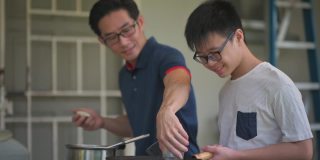 周末，一位亚洲华人父亲在自家后院的厨房教儿子做饭，准备晚餐