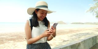 周末度假，亚洲美女在海边用智能手机拍照。快乐单人旅行的概念。