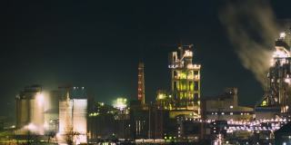 水泥厂高层混凝土结构，夜间有塔式起重机和烟筒。工业生产与空气污染的概念。