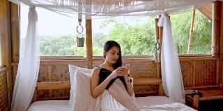亚洲女人在木制小屋的床上用智能手机度假